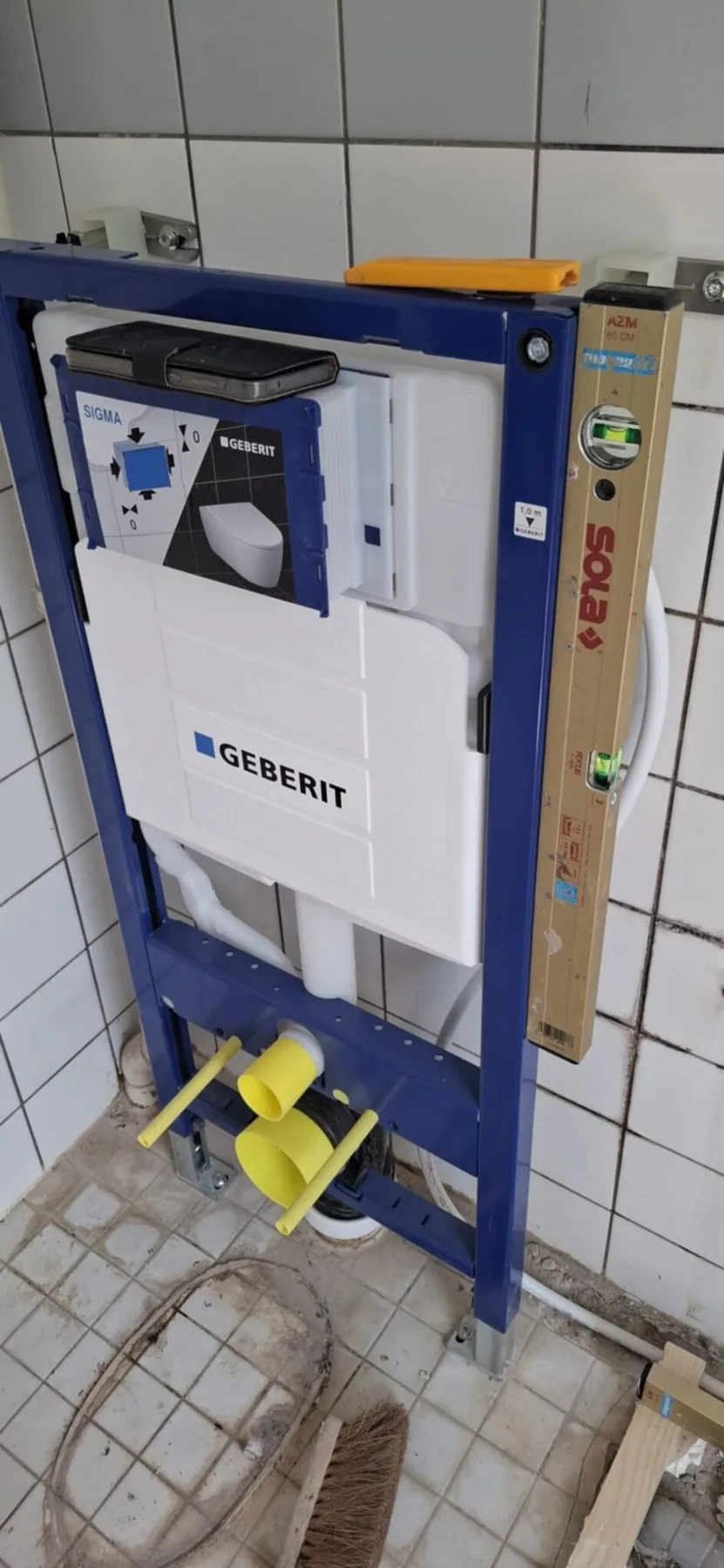 Inbouwreservoir in een blauw montageframe tegen een witte tegelwand, tijdens de montage