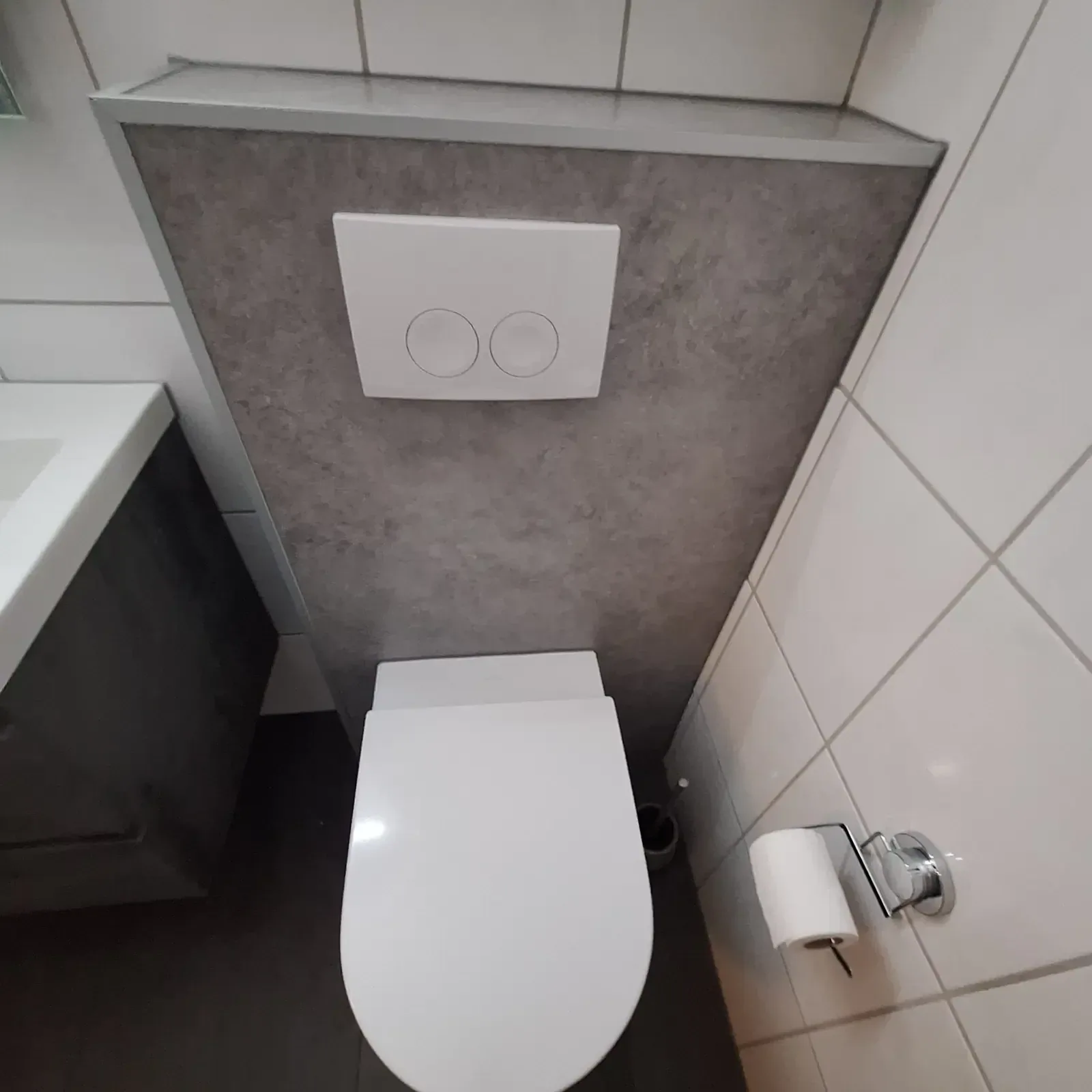 Hangtoilet met grijze steenlook voorzetwand, witte drukplaat en toiletrolhouder