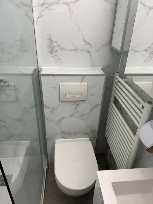 Wit hangtoilet op een voorzetwand met witte marmerlook wandpanelen en witte handdoekradiator