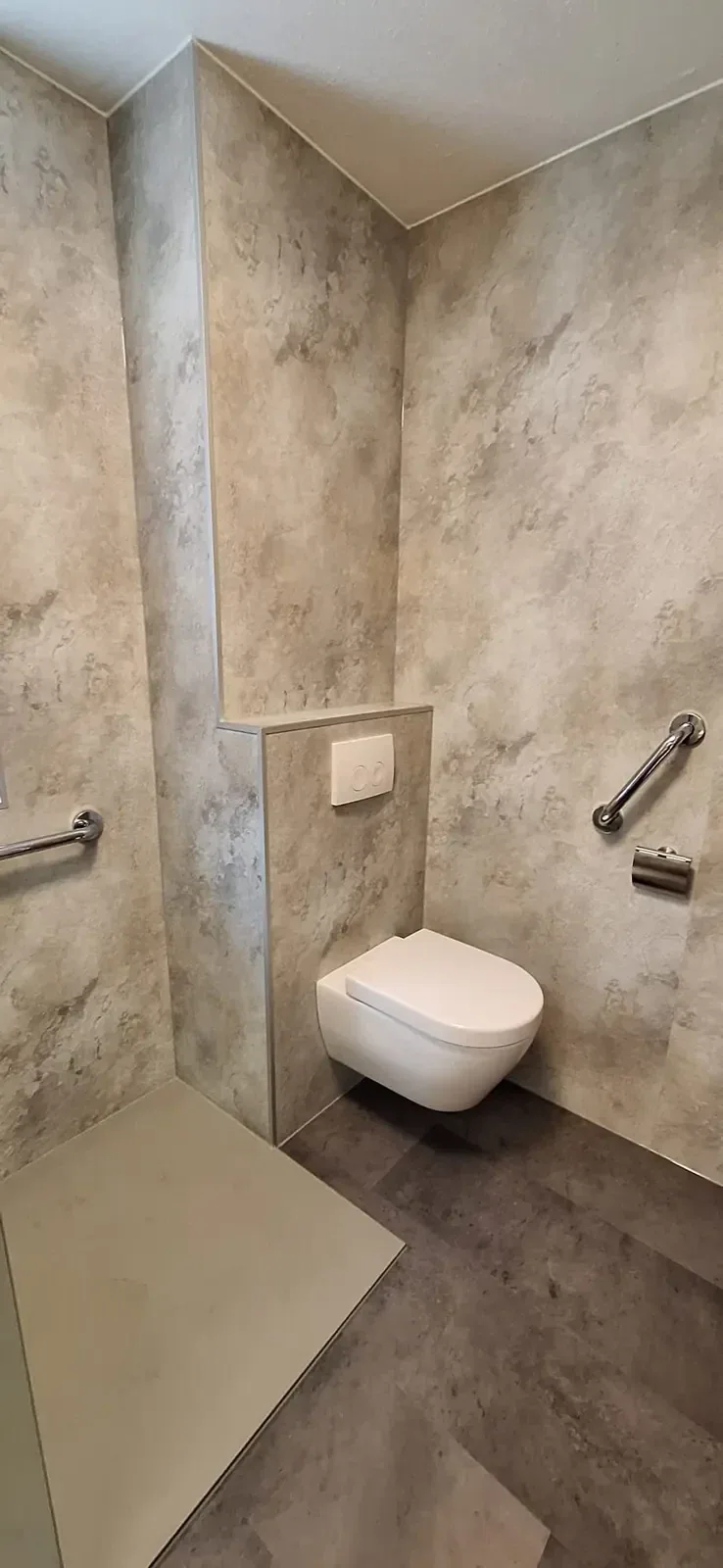 Hangtoilet op een voorzetwand met beige marmerlook wandpanelen en steunbeugels aan beide kanten