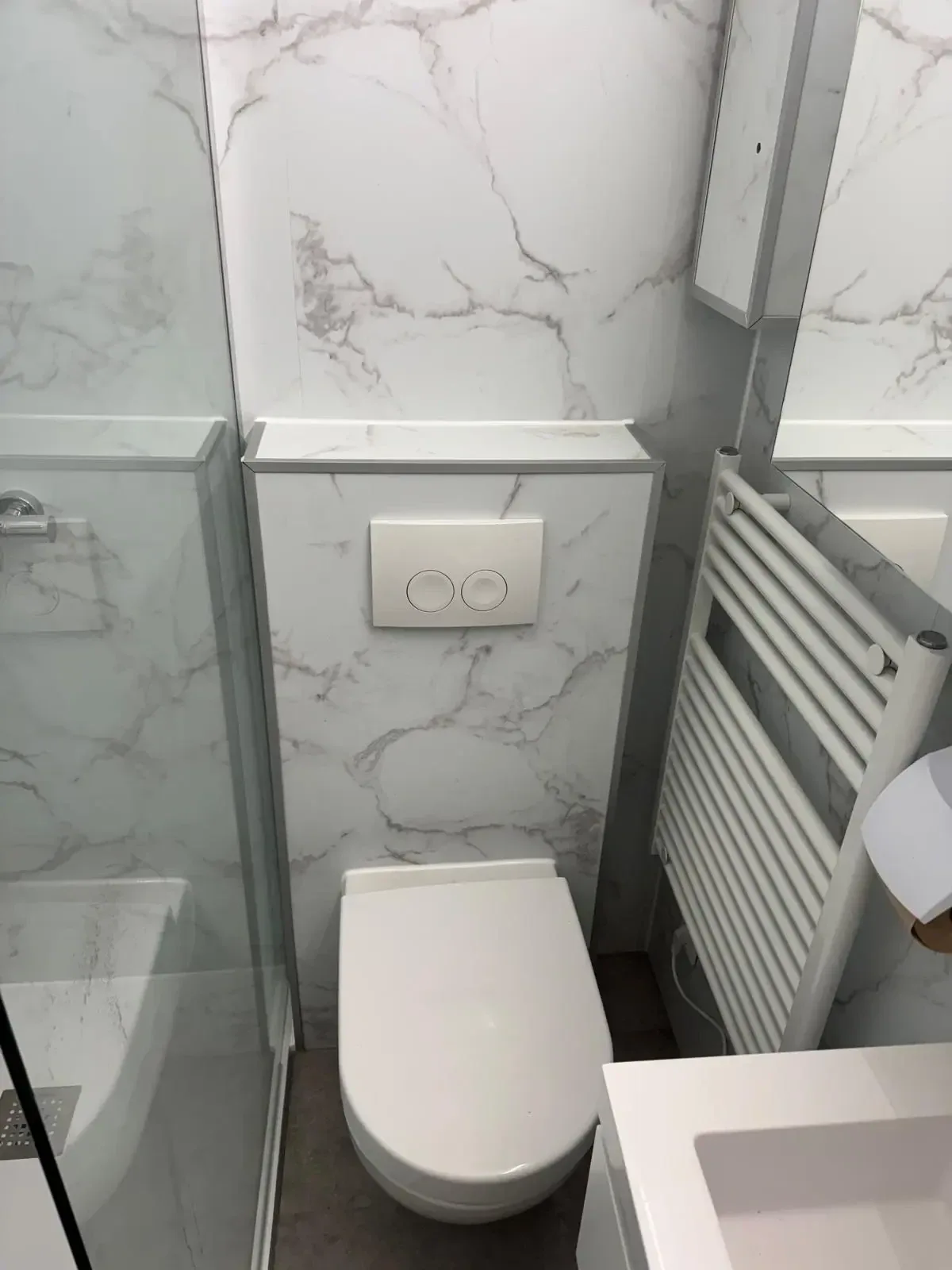 Wit hangtoilet op een voorzetwand met witte marmerlook wandpanelen en witte handdoekradiator