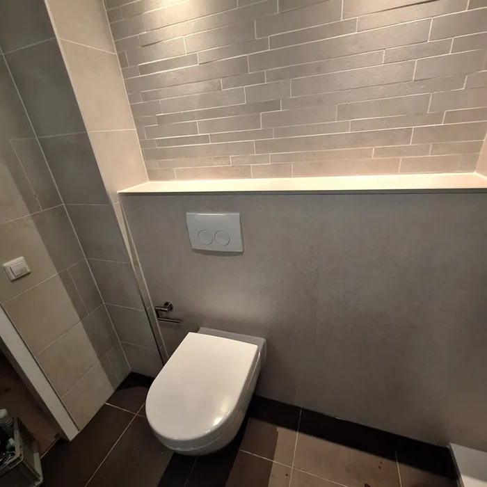 Hangtoilet tegen een grijze voorzetwand met verlichte nis en strokenwand erboven