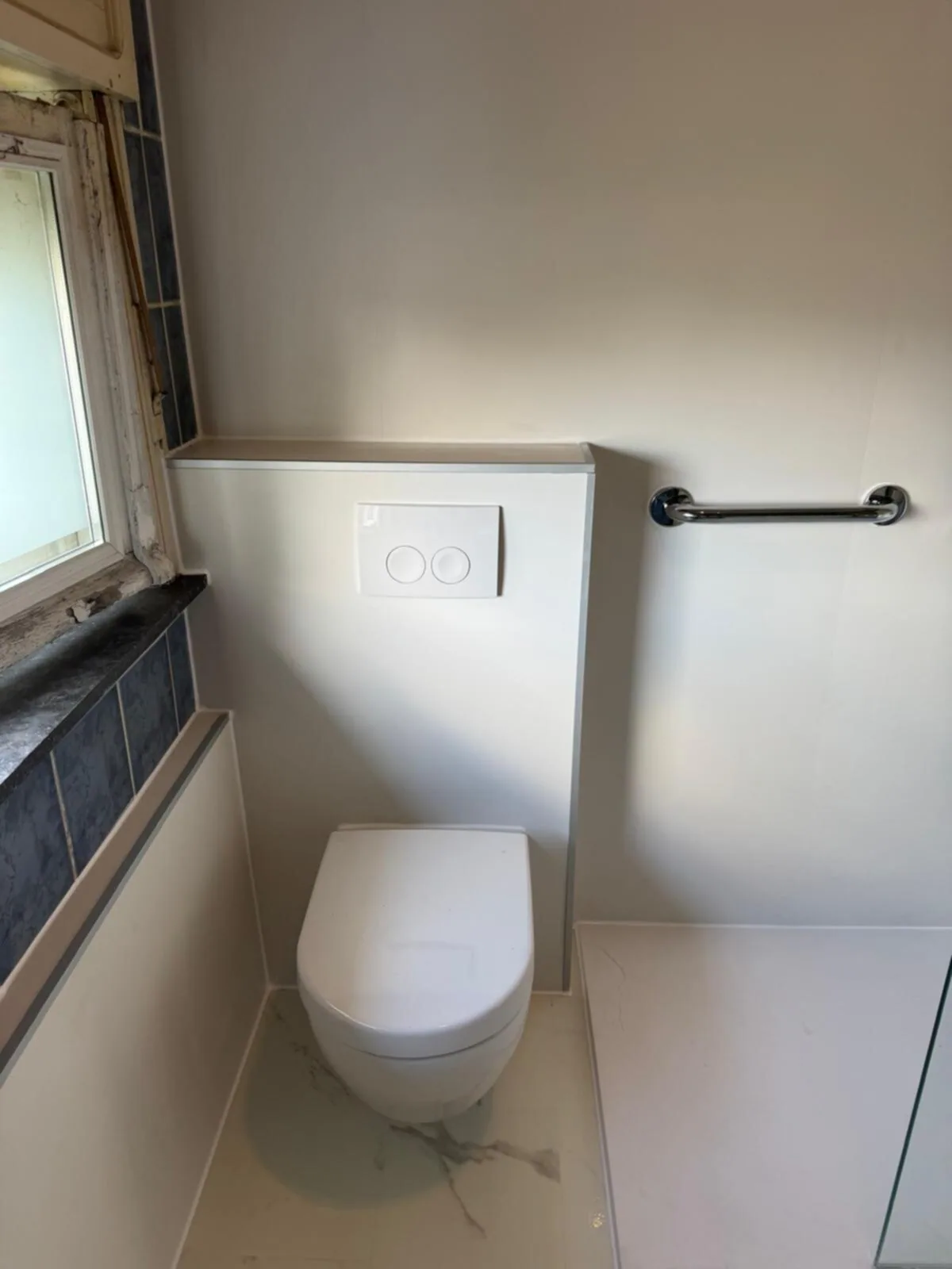 Hangtoilet tegen een witte voorzetwand met drukplaat, steunbeugel en een vloer in marmerlook