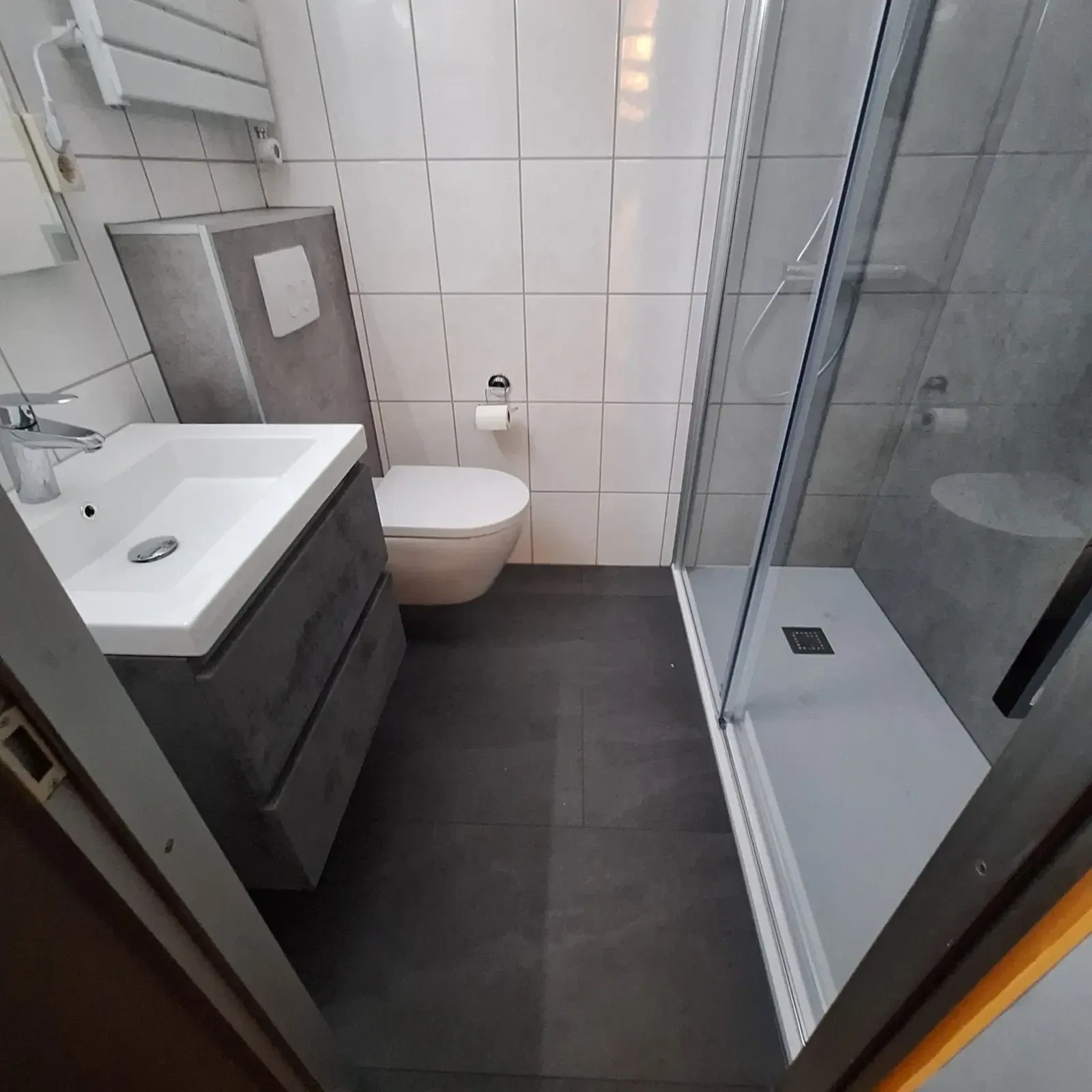 Kleine badkamer met wastafelmeubel, hangtoilet, douche met schuifdeur en donkere vloertegels