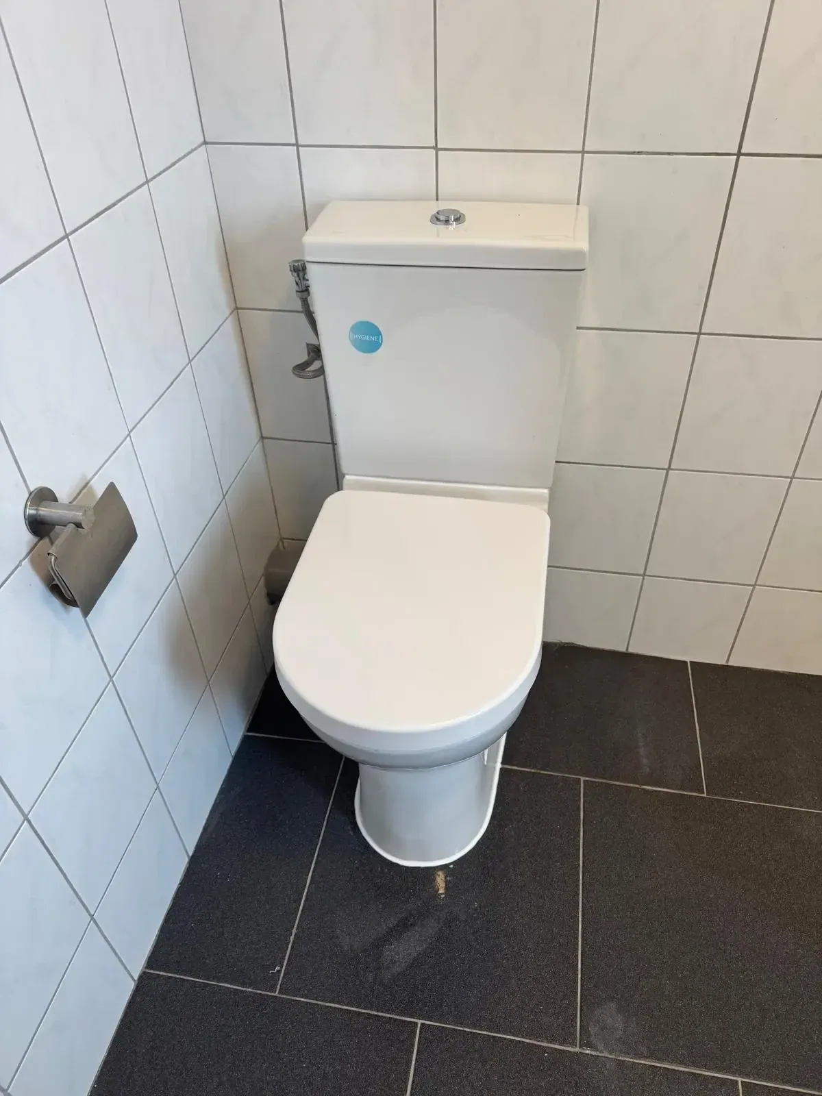 Nieuw wit staand toilet met duoblok tegen witte wandtegels op een donkere tegelvloer