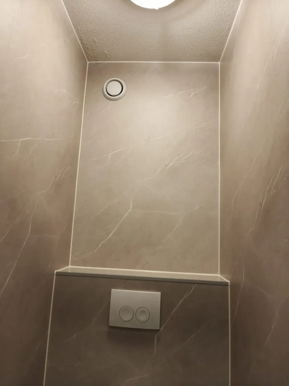 Toiletruimte met beige marmerlook wandpanelen en een voorzetwand met drukplaat en ventilatierooster