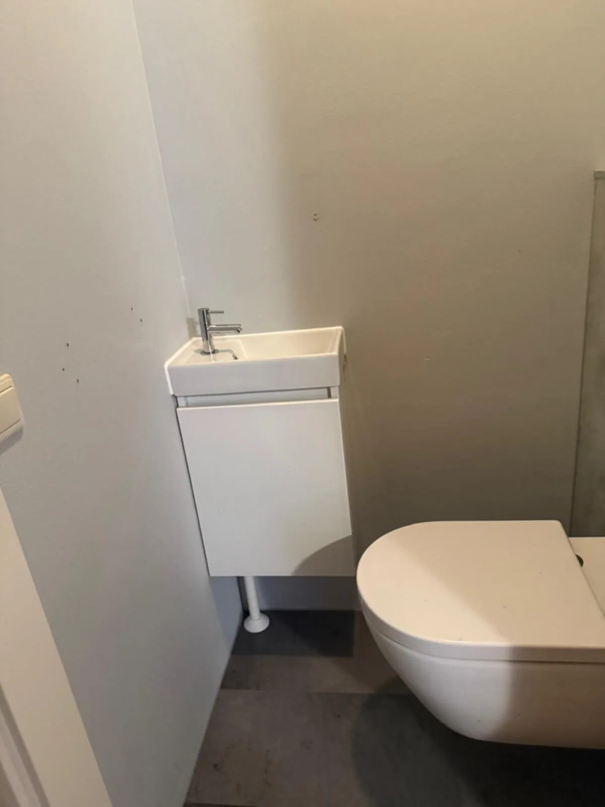 Toiletruimte met wit fonteinmeubeltje en wit hangtoilet op een donkere vloer