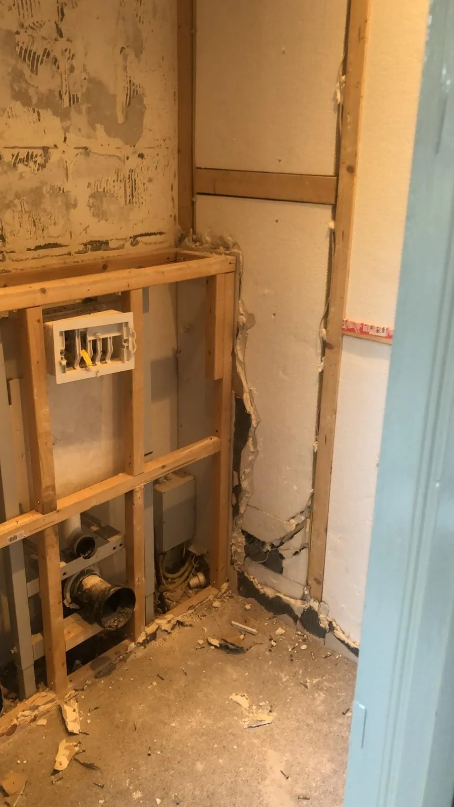 Gesloopte toiletruimte met houten regelwerk, oud inbouwreservoir en zichtbare afvoer