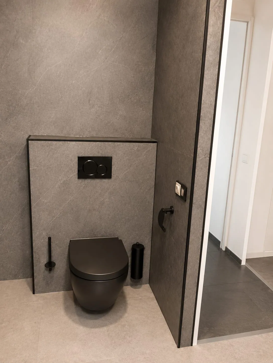 Zwart hangtoilet tegen een grijze voorzetwand met zwarte drukplaat