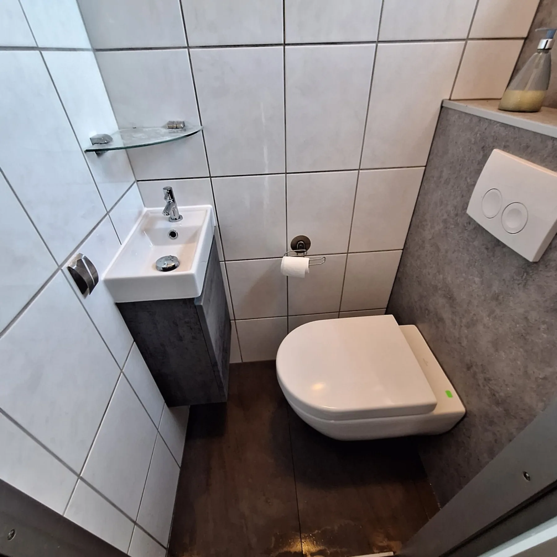 Klein toilet met hangtoilet, grijze voorzetwand met drukplaat, fonteintje met meubel en houtlook vloer