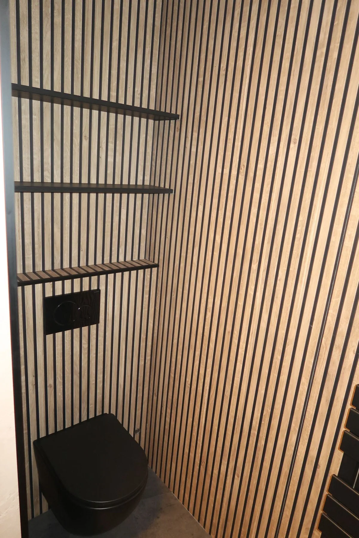 Toiletruimte met houten lamellenwand, zwart hangtoilet en zwarte planken