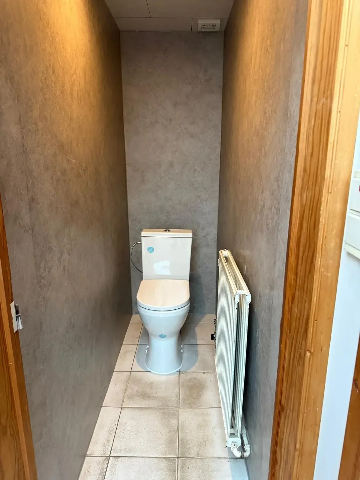 Smalle toiletruimte met wandpanelen in betonlook, een staand toilet en een radiator