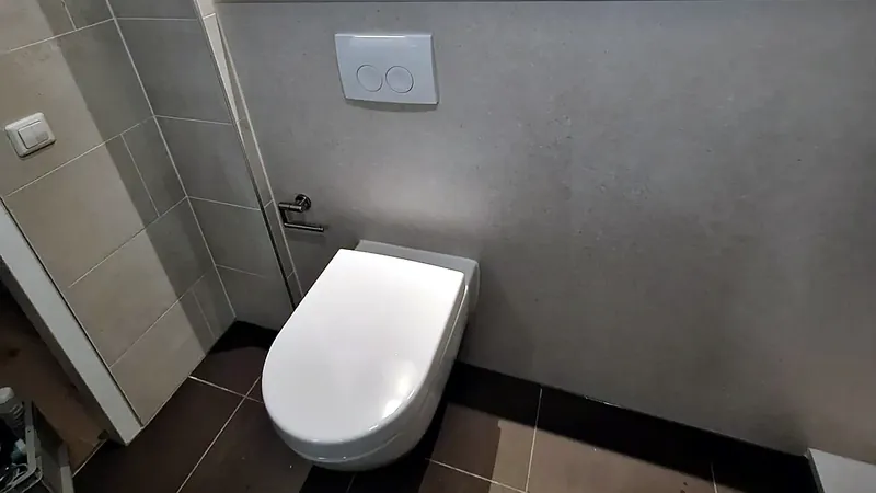 Hangtoilet onder een verlichte wandnis met grijze tegelstrook