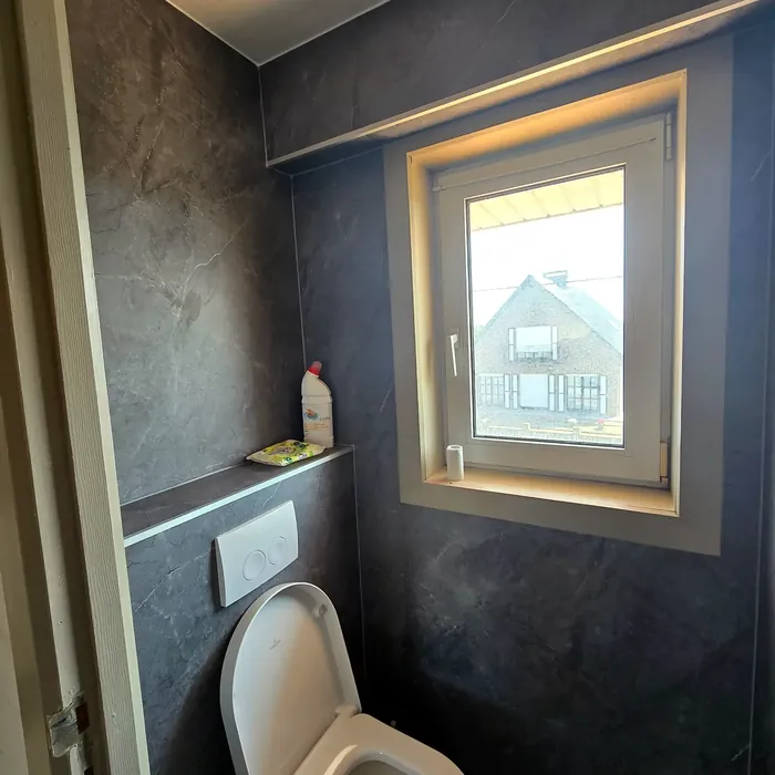 Toiletruimte met donkere natuursteenlook wandpanelen rond het raam