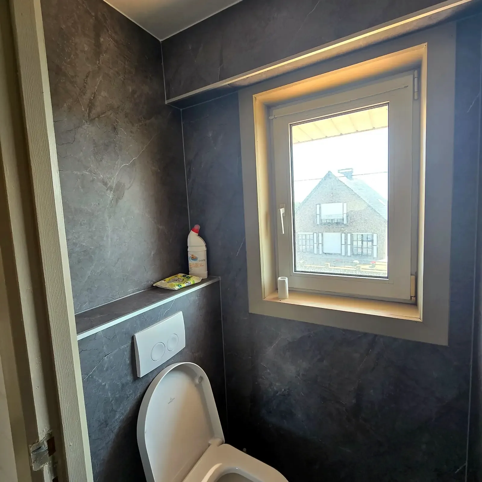 Toiletruimte met donkere natuursteenlook wandpanelen rond het raam