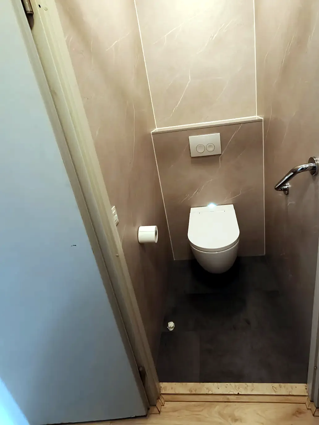 Smalle toiletruimte afgewerkt met taupe marmerlook wandpanelen en hangtoilet