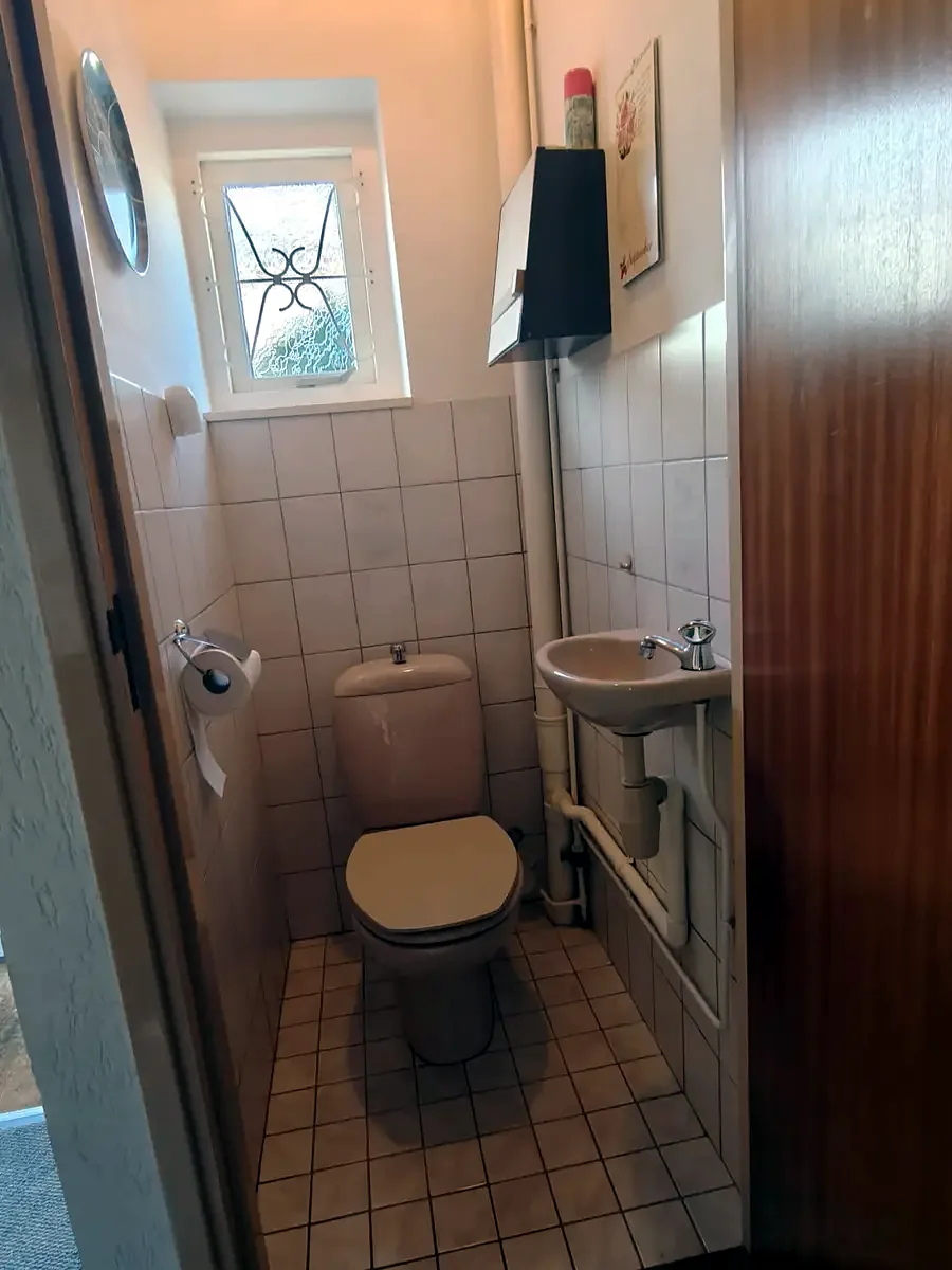 Smal toilet met sierraam, wit tegelwerk en staand toilet vóór de renovatie