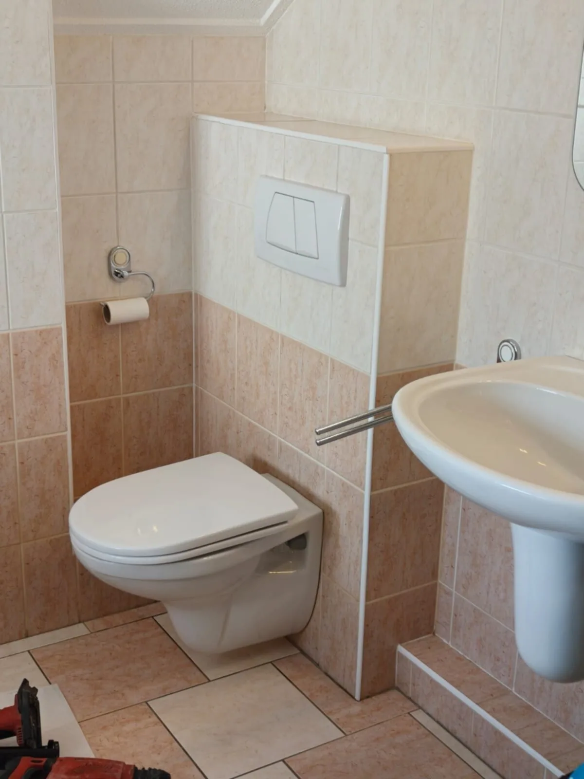 Oude situatie: hangtoilet tegen een betegelde voorzetwand met beige-roze tegels