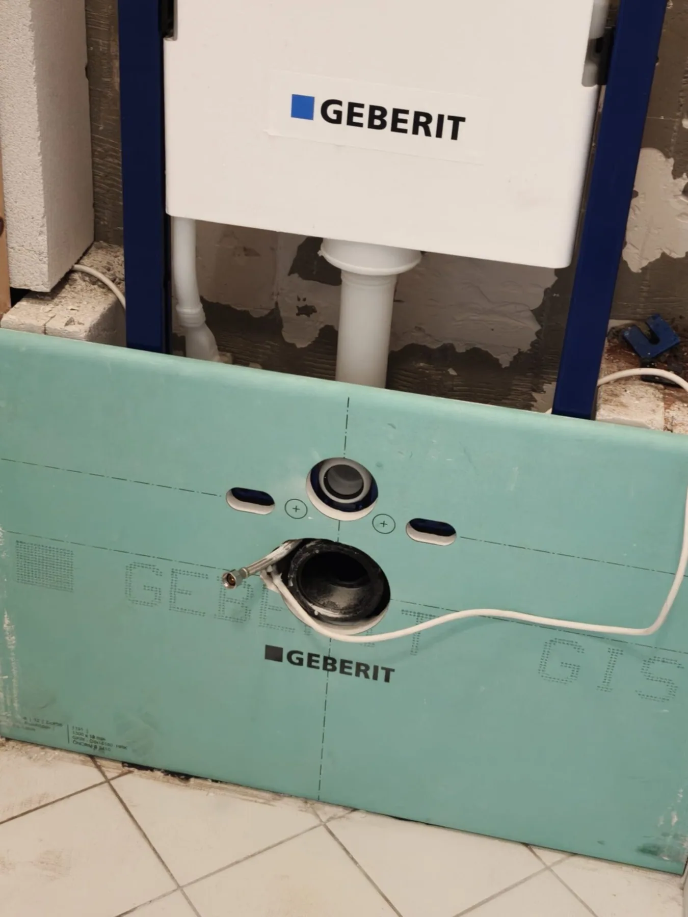 Close-up van het inbouwreservoir met groene voorzetwandplaat en aansluitingen voor het hangtoilet