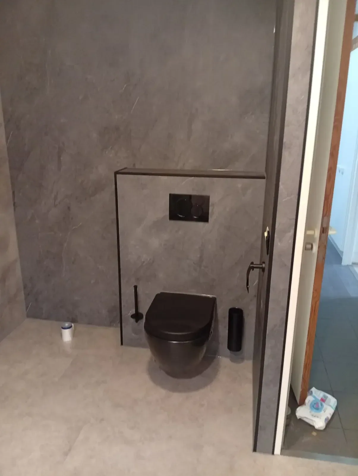 Zwart hangtoilet voor een grijze steenlook voorzetwand met zwarte drukplaat